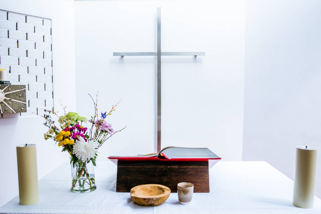 Close up altaartafel met bijbel en bloemen, tegen achterwand het kruis.